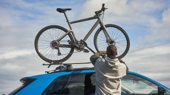 Mann befestigt Fahrrad auf Dachträger eines blauen Audi.