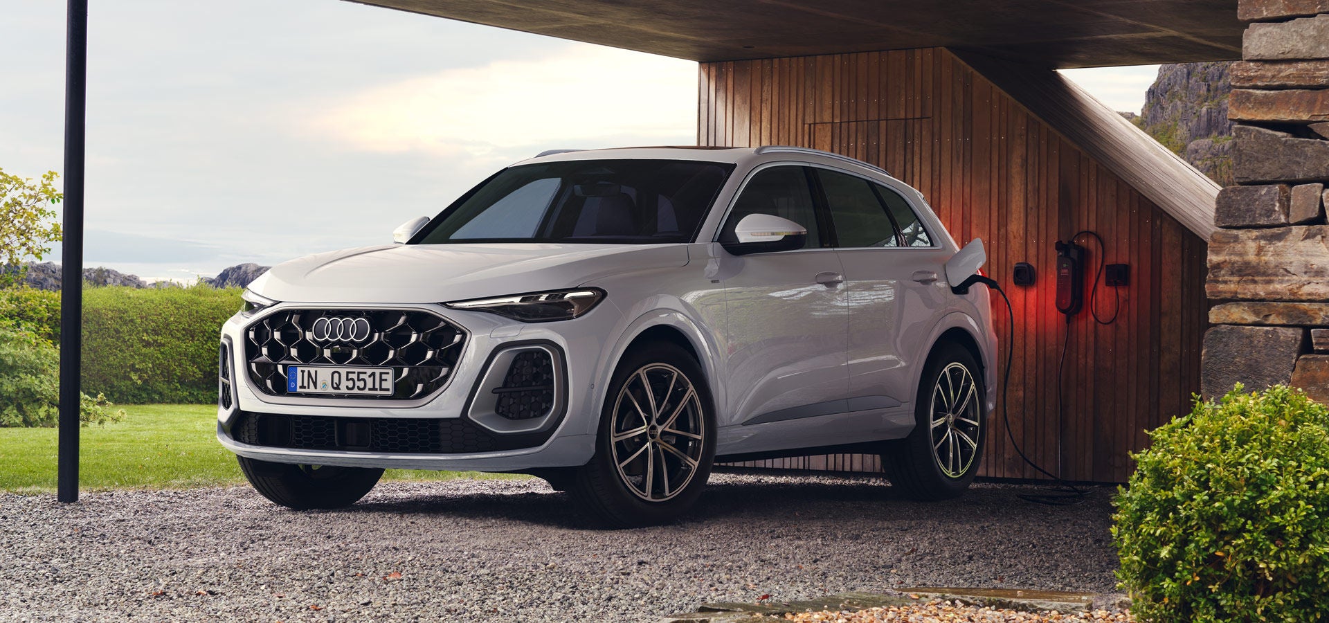 Ein weißer Q5 SUV e-hybrid in schräger Frontansicht ist unter einem Carport an eine Ladestation angeschlossen.