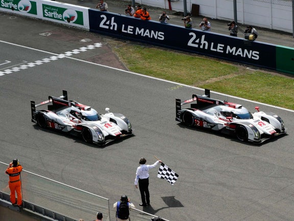 A picture showing the Audi R18 e-tron quattro race cars crossing the finish line at the 2014 Le Mans 24 Hours.
