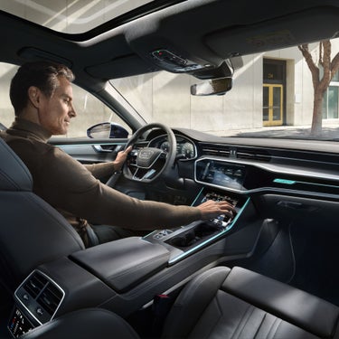 Person driving a car interior with sleek dashboard and touchscreen controls.