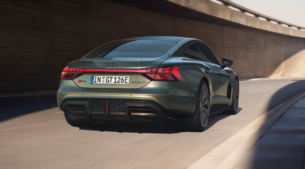 Um Audi RS e-tron GT performance verde, visto por trás, numa estrada sinuosa sob uma ponte de concreto.