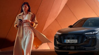 Vrouw met smartphone naast een 100% elektrische Audi voor moderne architectuur, die symbool staat voor elektrische mobiliteit in de stad en vooruitstrevend design.