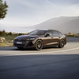 Blick auf die Front des A6 Avant, während das Fahrzeug auf einer kurvigen Landstraße an der Küste entlangfährt.