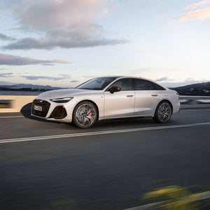 Seitliche Aufnahme der A6 Limousine e-hybrid in weiß, welche auf einer Straße entlang der Küste fährt. Am Steuer sitzt ein junger Mann.