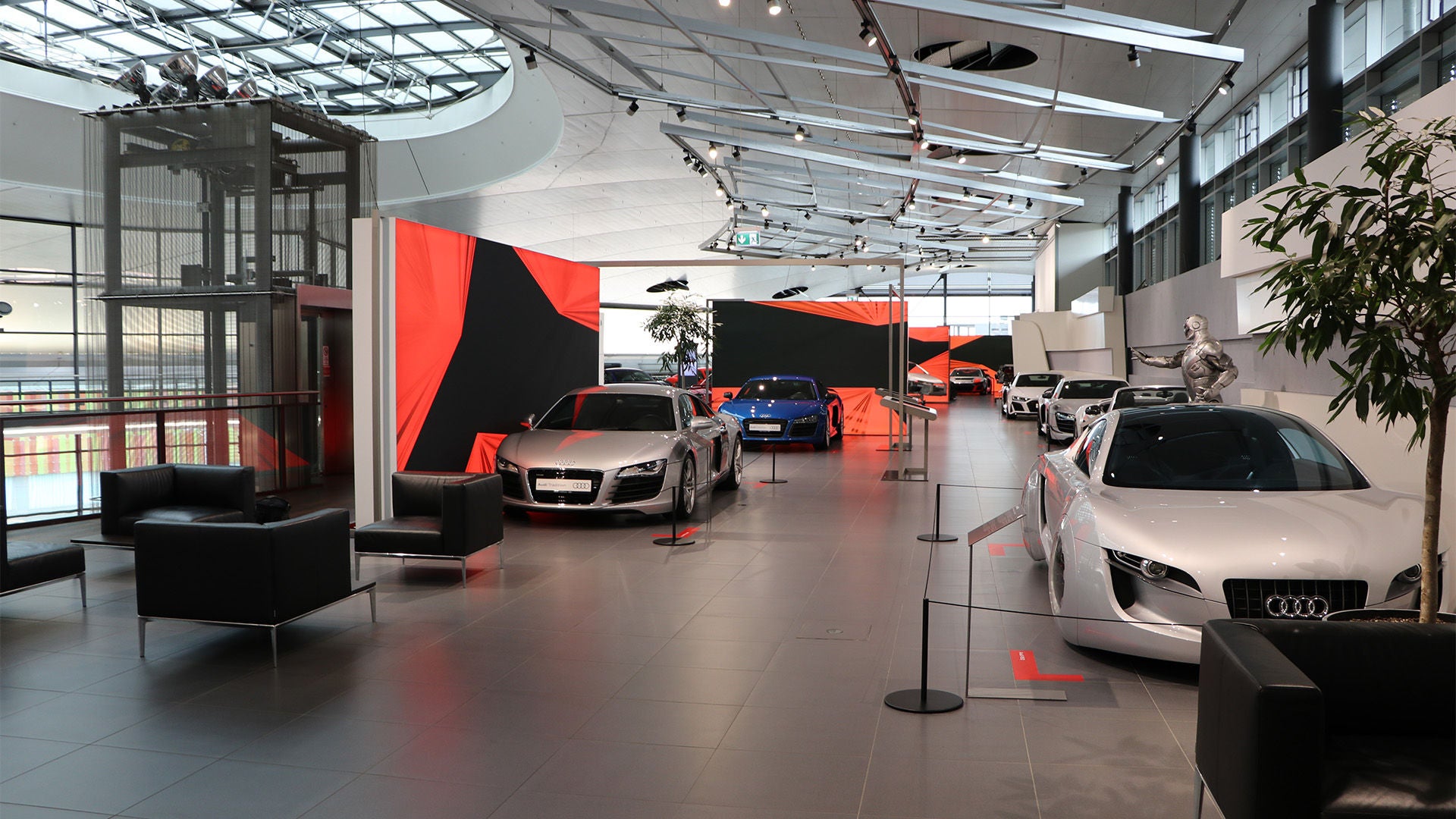 Interior of an Audi exhibition space, with several sports cars, modern architecture, lounge areas and striking red and black design elements.