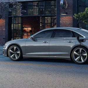 A silver Audi car charges outside a brick building with large windows, reflecting modern urban style and sustainability.