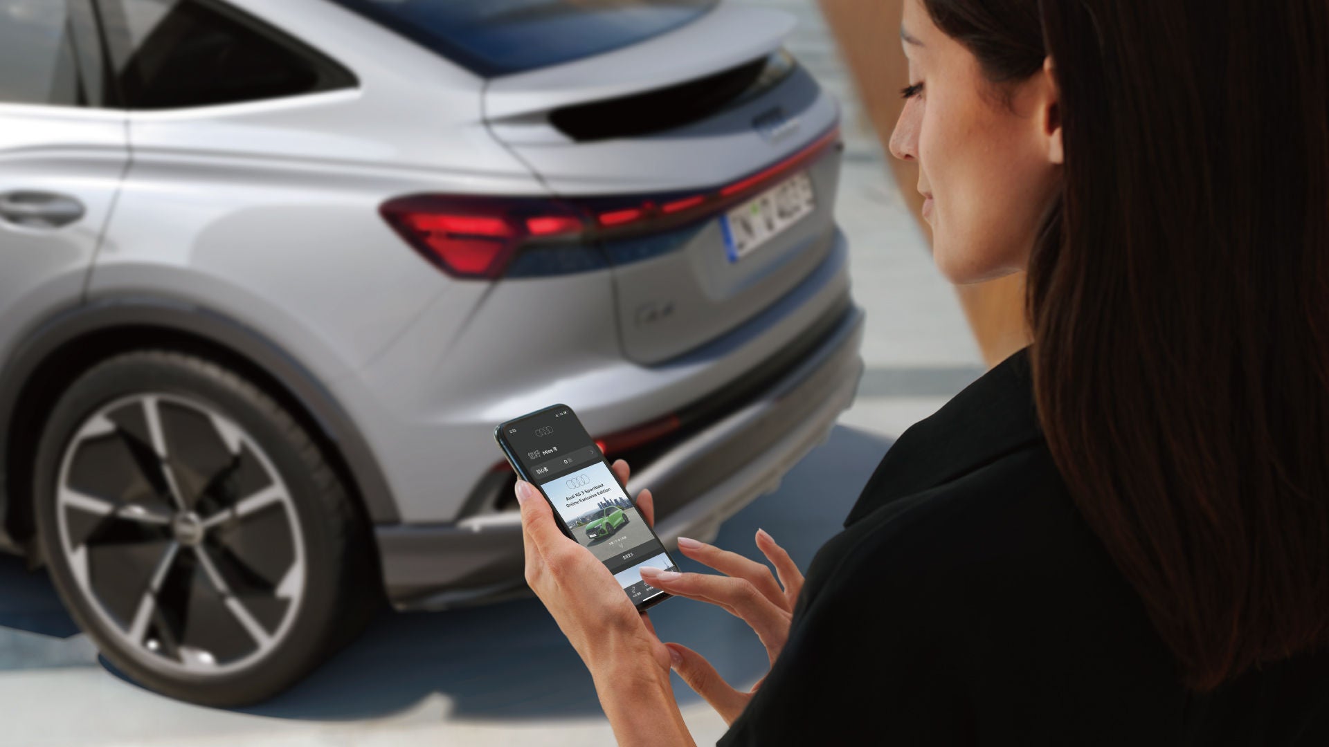 Frau steht neben einem silbernen Audi Q4 e-tron und bedient eine App auf ihrem Smartphone