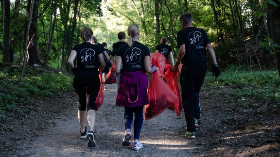 Group of joggers with red rubbish bags on a forest path.