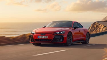 Der e-tron GT quattro auf einer kurvigen Küstenstraße bei Sonnenschein, zur Linken das Meer, zur Rechten felsiges Gebirge. 