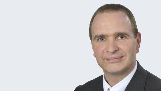 Heiko Kübler: Porträt eines älteren Mann im Anzug vor grauem Hintergrund.