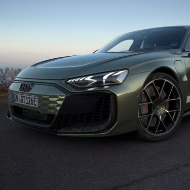 A green Audi sports car with angular headlights and a sporty grille, parked against a scenic city backdrop.