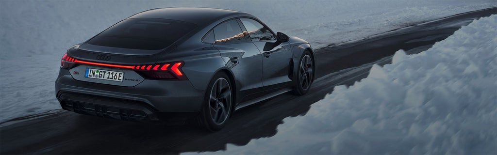 An Audi vehicle, back lights lit, driving on a road with snow piles on either side of the road