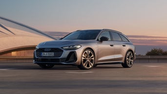 A metallic Audi vehicle parked in front of a modern building with a sunset background