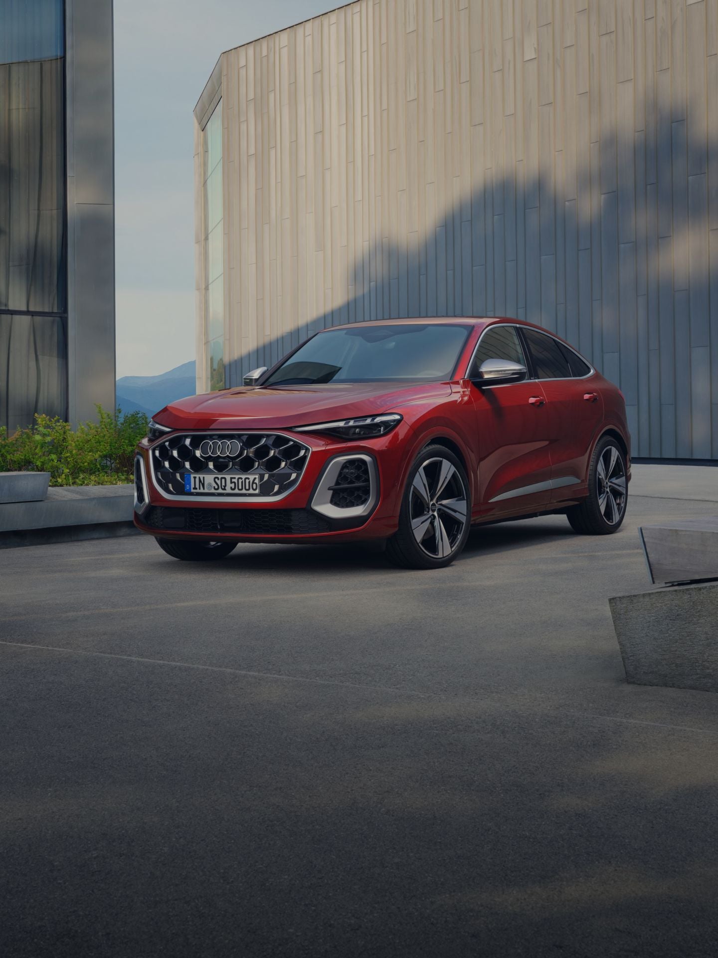 A red Audi SQ5 Sportback parked outside, surrounded by a modern building and some greenery.