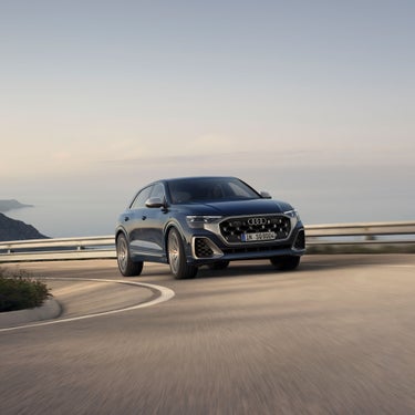Audi SUV climbing uphill on a coastal road.