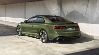 Grüner Audi A5 Coupé von schräg hinten in heller Tiefgaragenumgebung mit glatten Betonwänden und Schatten.