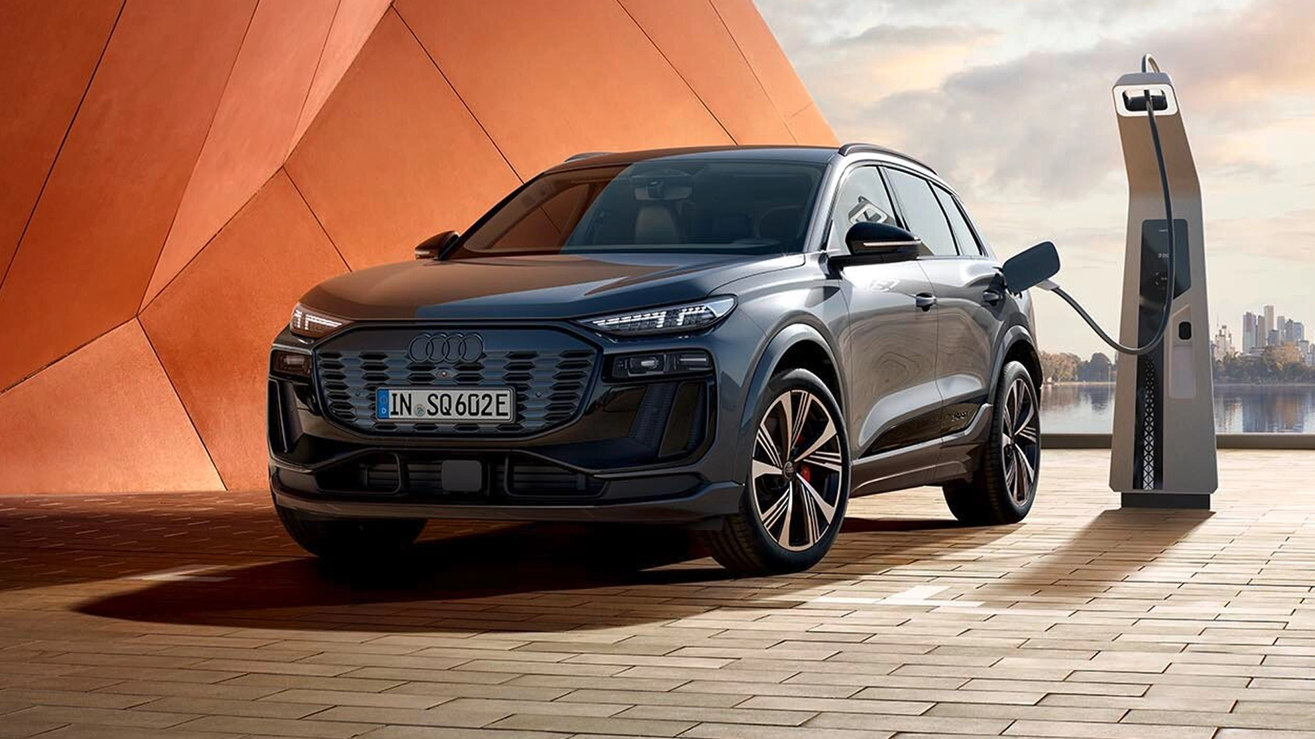 The Q4 Sportback e-tron is parked in front of a modern building facade and is connected to a charging station.