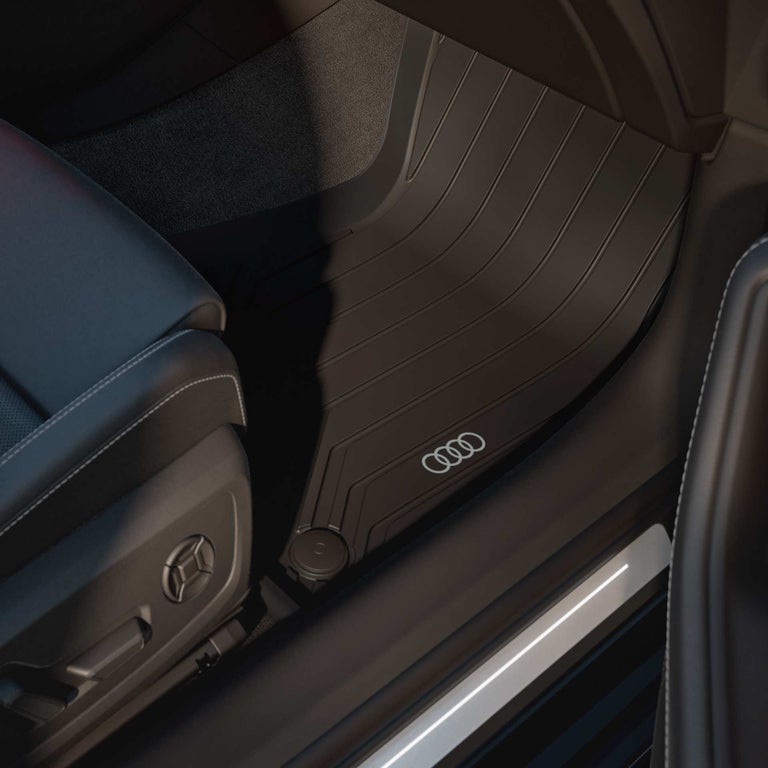 Schwarze Gummifußmatte mit Audi-Ringen im Fußraum einer Audi A6 Limousine, umgeben von dunklem Leder.