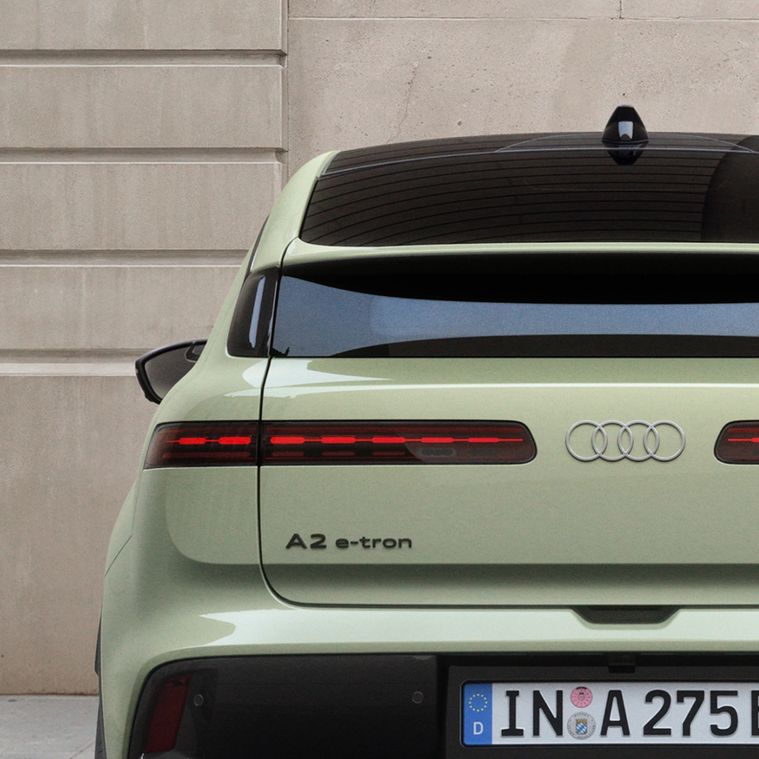 Pistachio green Audi A2 e-tron electric hatchback parked on a city street next to a modern stone building