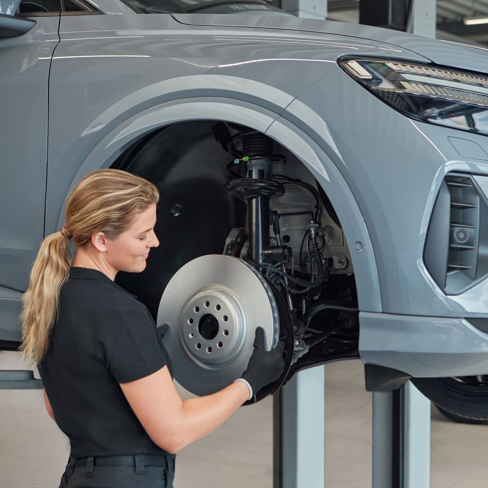 Eine Frau führt eine Bremsenwartung an Audi auf der Hebebühne durch.