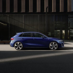 Een blauwe A3 Sportback staat geparkeerd voor een glazen wand.