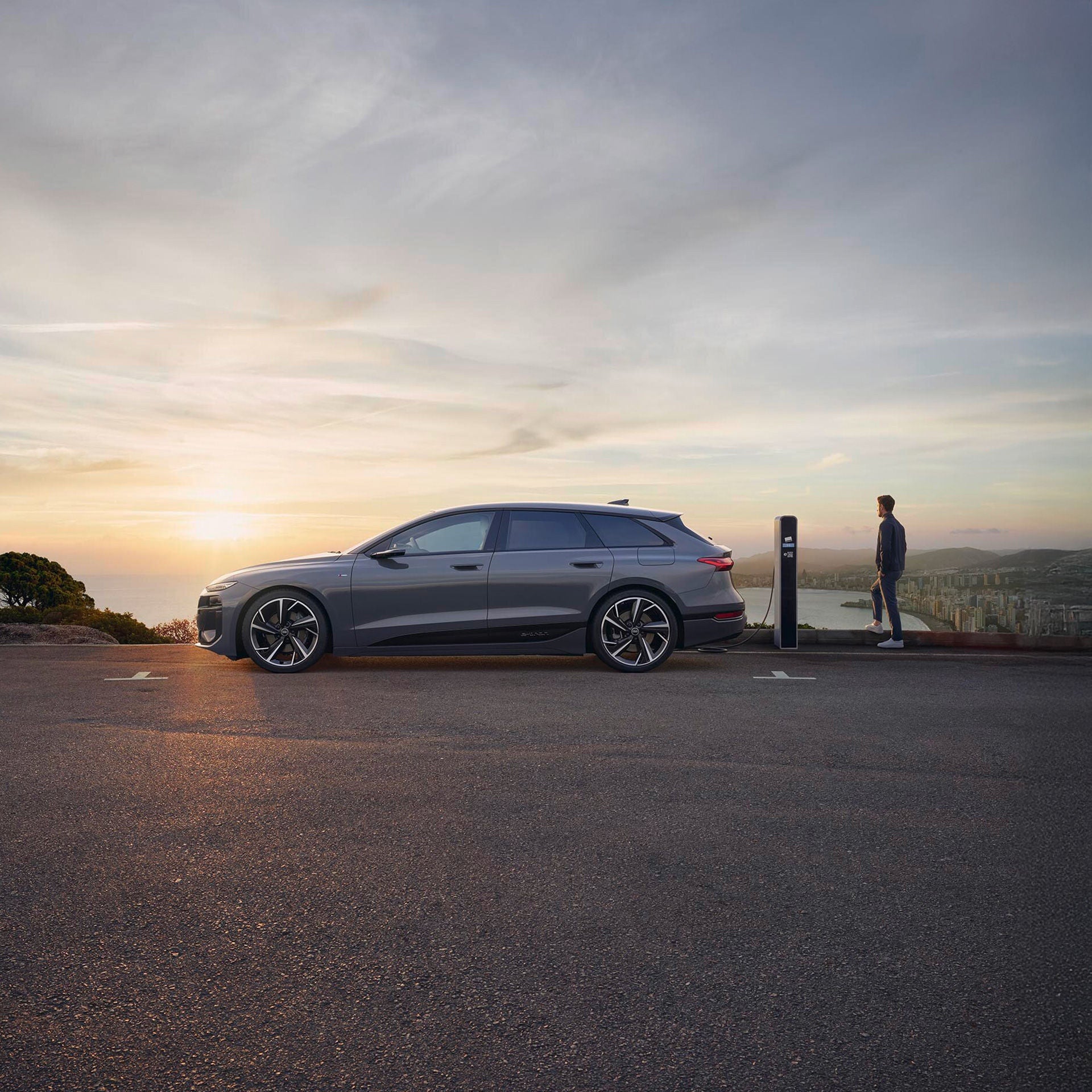 Auto steht im Sonnenuntergang an einer Ladestation und ein Mann steht neben diesem