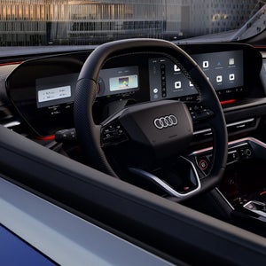 Zicht door het bestuurdersraam op de cockpit van de Audi SQ5 SUV. De focus ligt op het stuur, met de Audi virtual cockpit erachter en het MMI-touchdisplay.