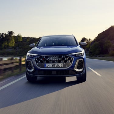 Frontprofil des SQ5 SUV in dunkelblau, welcher auf einer Straße durch die Natur fährt. Am Steuer sitzt eine junge Frau.&nbsp;