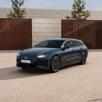 Ein graublauer A6 Avant e-tron von schräg vorne fotografiert vor einer modernen Kulisse.
