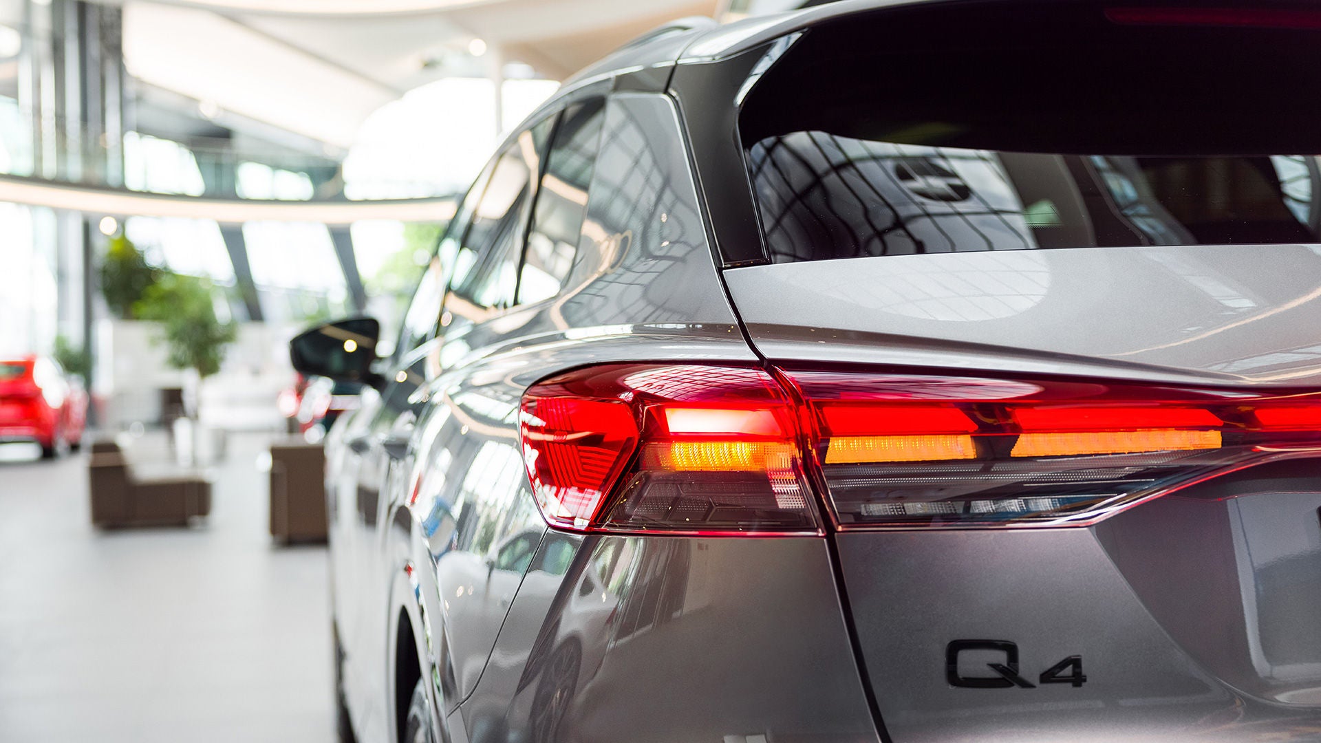 Rückansicht eines silbernen Audi Q4 in einem modernen Ausstellungsraum mit hellen Glasfassaden und anderen Fahrzeugen im Hintergrund.