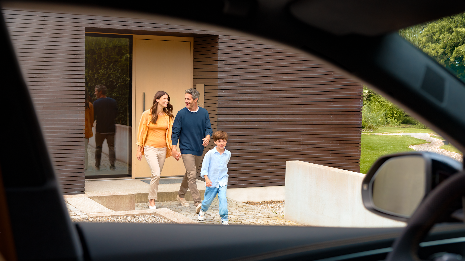 En familie på vej ud af et hus set fra et bilvindue