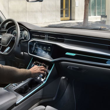 Interior of a car with touchscreen controls and ambient lighting, driver's hand adjusting settings.