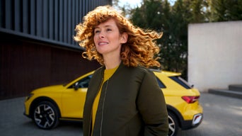 A  woman is walking. An Audi model is parked in the background.