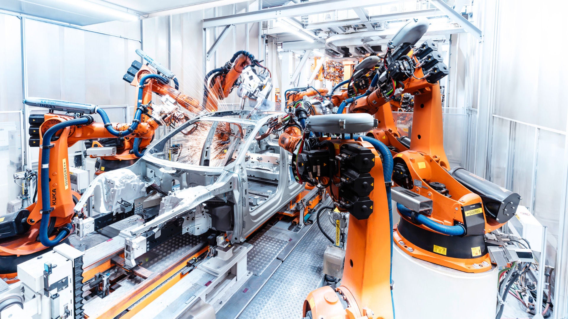 Robotic arms weld a car body in a brightly lit, automated production line.