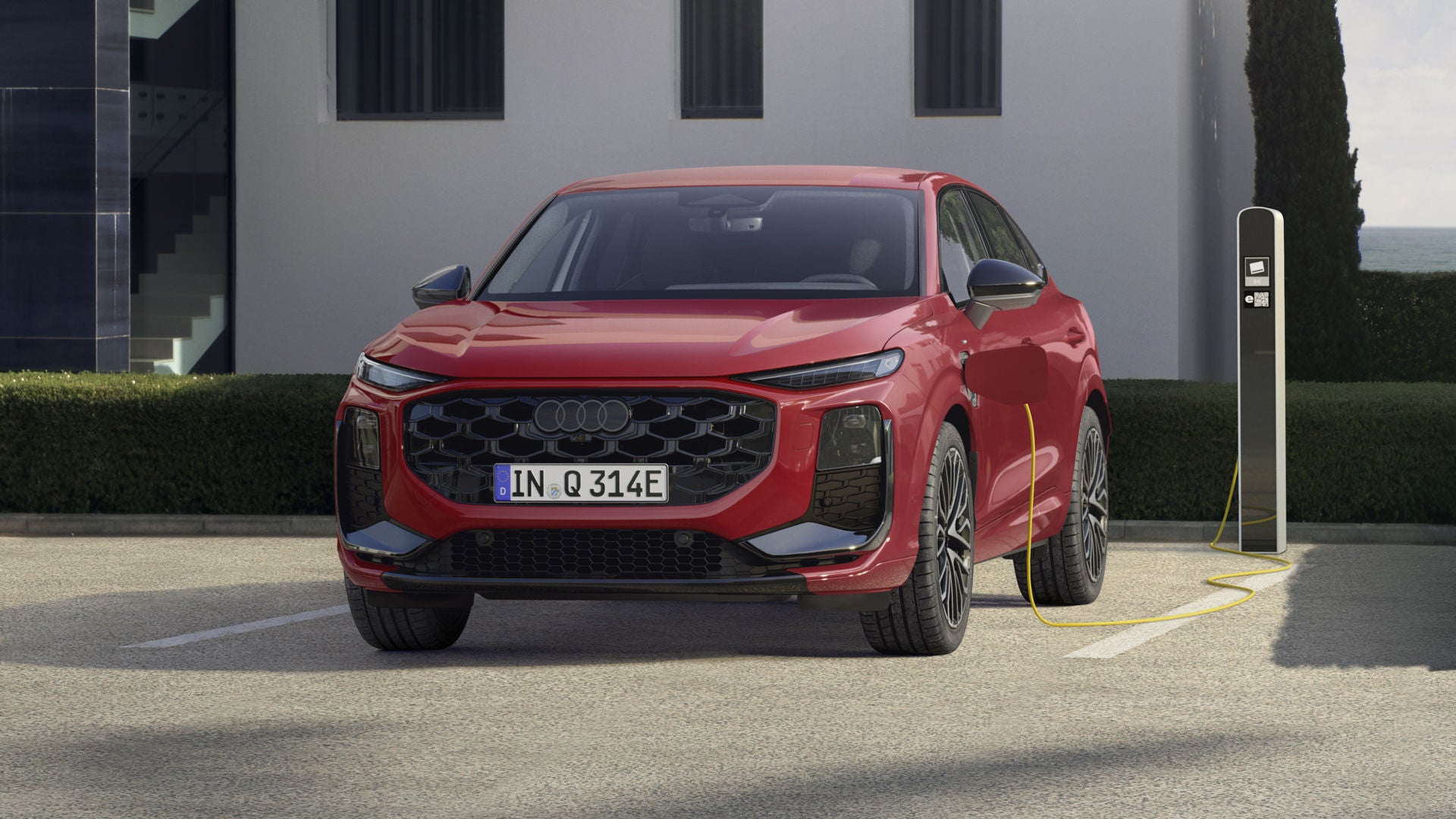 Ein roter Q3 Sportback e-hybrid parkt vor einer Ladesäule und wird mit Strom betankt.