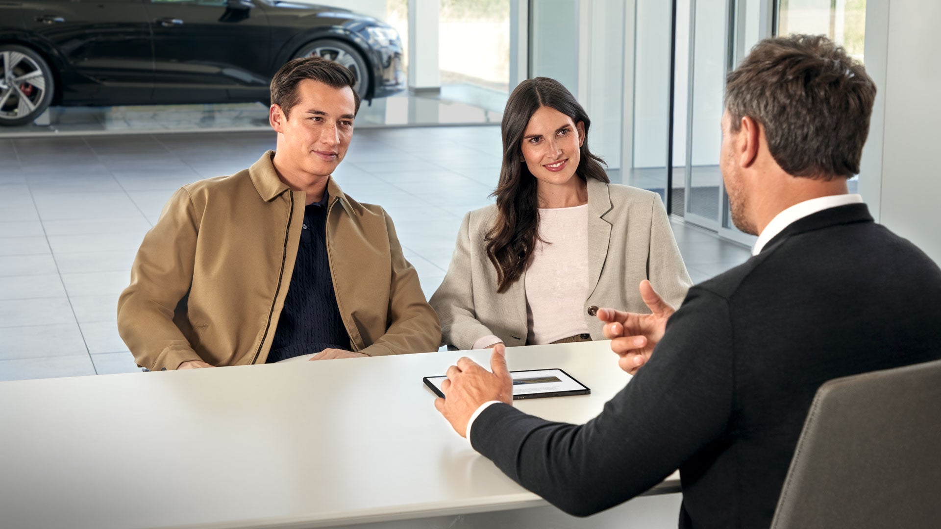 EIn Mann und eine Frau sitzen mit einem Audi Verkäufer an einem Tisch