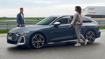 Eine Frau steigt in ein Fahrzeug der Audi driving experience ein. Der Fahrinstrukteur steht neben dem Fahrzeug an der Beifahrerseite.
