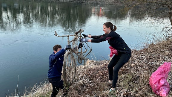 Zwei Personen heben ein Fahrrad aus dem Wasser