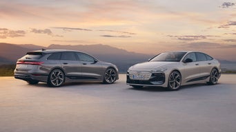 Zwei silberne Audi e-tron Modelle bei Sonnenuntergang mit Bergkulisse im Hintergrund.