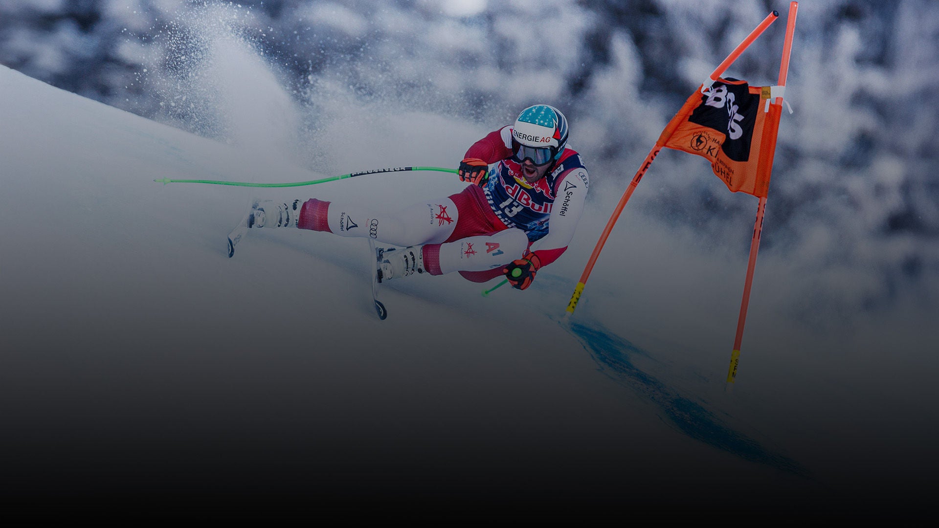 Skirennfahrer im Slalom fährt mit hoher Geschwindigkeit durch ein Tor, Schnee spritzt auf, dynamische Bewegung im winterlichen Umfeld.