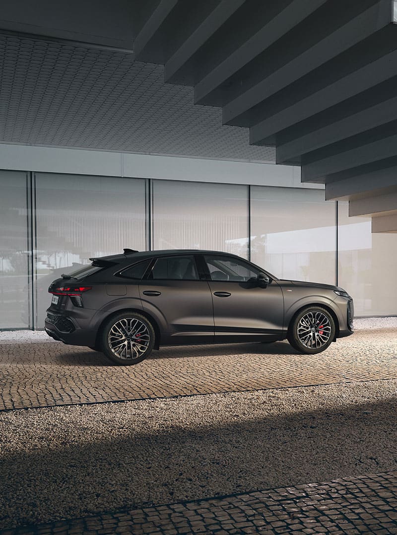 The Audi Q3 Sportback stands in a dim light under a staircase. The car can be seen from the side, showing the exact details of the exterior.