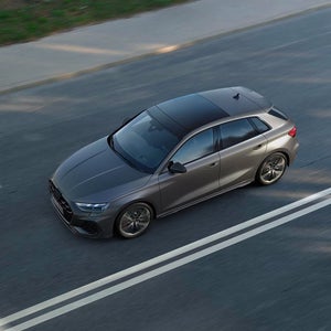 Aerial view of a grey Audi S3 Sportback driving on a dual-lane road, showcasing its modern design and glossy finish.