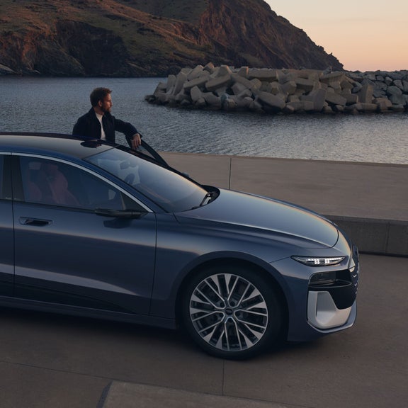 A sleek grey car parked on a pier near the ocean at dusk.