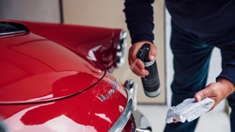 Eine Hand sprüht mit dem Insektenentferner von Audi auf das Emblem eines Audi Oldtimers