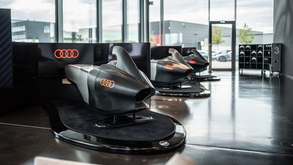 Drei Audi racing Simulator stehen hintereinander auf runden Plattformen im hellen Showroom.