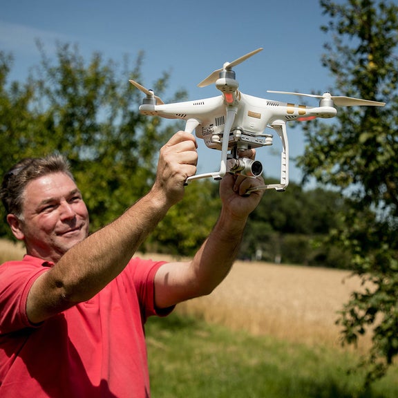A man in a red T-shirt launches a drone in a meadow orchard.
