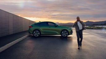 Grüner Audi Q5 Sportback in Seitenansicht bei Sonnenuntergang, lächelnder Mann geht am Auto vorbei.