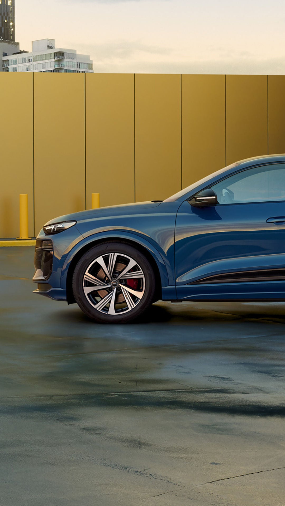A blue Audi SQ6 Sportback e-tron parked in an open space with yellow building at the back