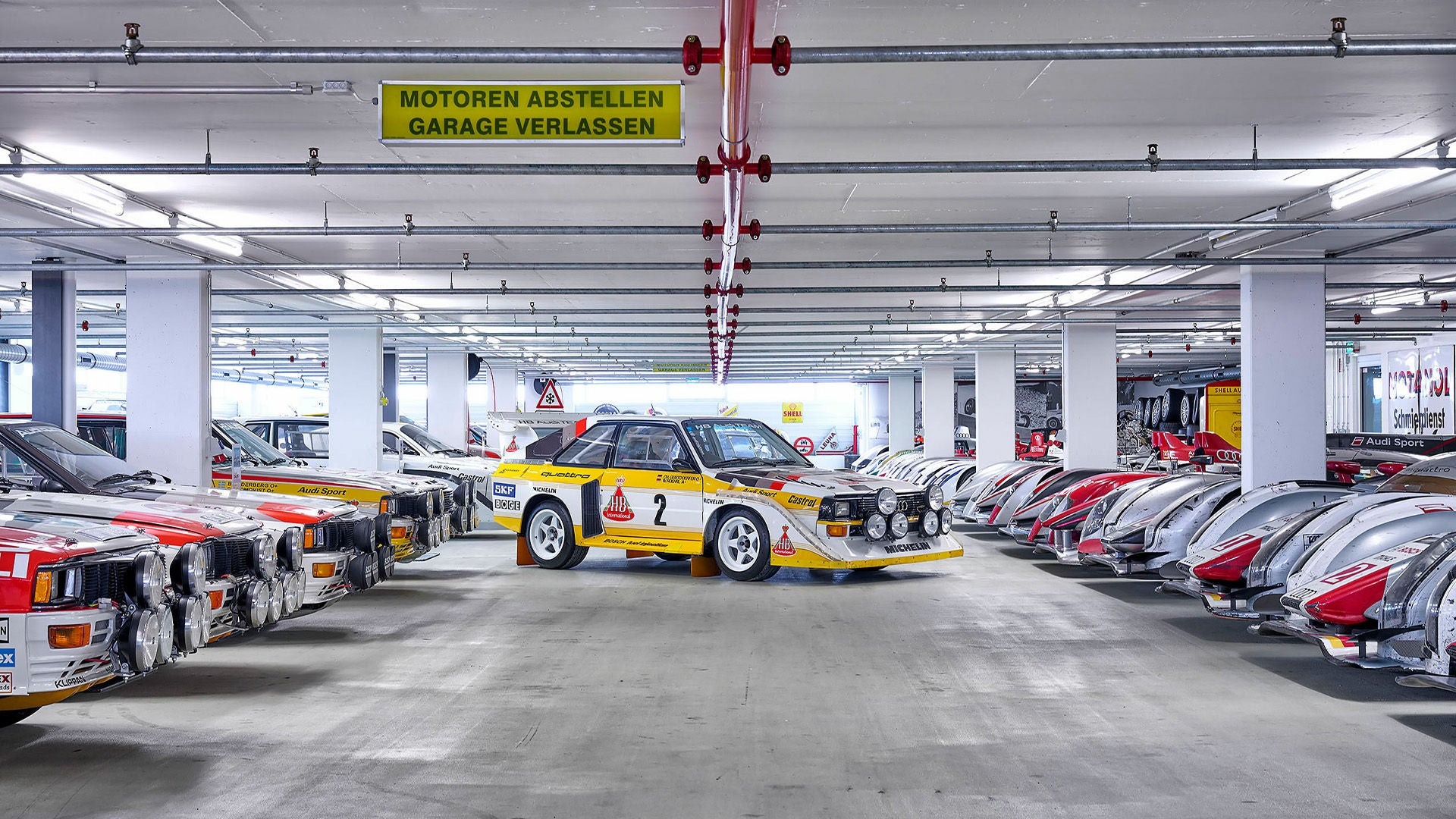 A classic Audi Quattro racing car in a garage, surrounded by other Audi racing cars.