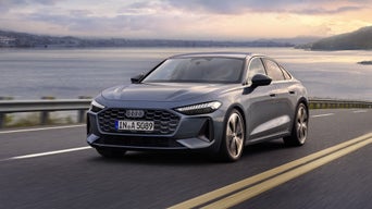 Die A5 Limousine im schrägen Frontprofil. Das Fahrzeug fährt auf einer Straße entlang der Küste. Im Hintergrund beginnt die Dämmerung.